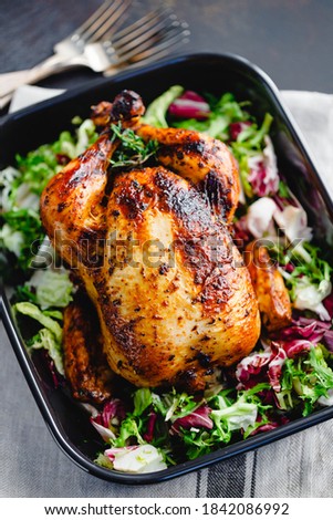 Top view of a whole roasted chicken served with fresh salad in black pan. Thanksgiving or family dinner celebration cooking concept.