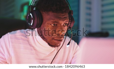 Happy young black man with illuminated headset using laptop. Home office and remote work concept. Stock trader portrait. High quality photo