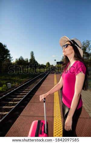 A wealthy adult teenager in a hat waits for a train on a railway platform. The summer adventure begins with waiting for the train.