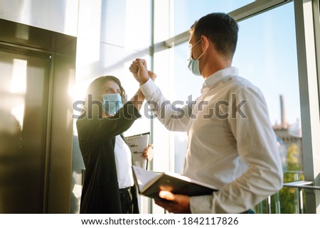 Two colleagues in protective sterile mask bumping elbows while greeting each other at work in modern office. Business partners back at work in office after quarantine. Covid-19. Royalty-Free Stock Photo #1842117826