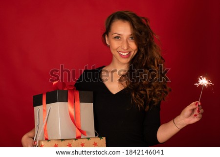 Cheerful attractive woman celebrating New Year, Christmas, Hanukkah, Kwanzaa holiday. Lady with gift boxes and sparkler on red festive background. Holiday promotions discounts offers black friday sale