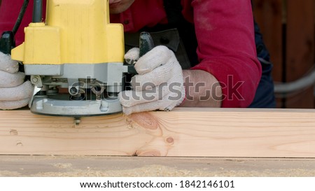 Caucasian carpenter processes wood beam with a milling machine in his carpentry workshop. The master rounds the corners of the beam using a milling machine. Production of craft wooden furniture.