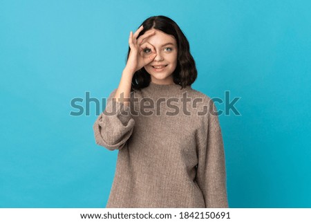 Teenager Ukrainian girl isolated on blue background showing ok sign with fingers