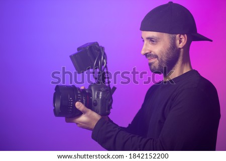 Man filming with his camera. Cameraman shooting with a Dslr and cinema lens. Professional videographer on a movie or music video set. Broadcast and cinematography concept. Purple background
