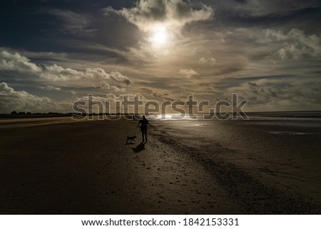 A silhouette of a lady walking a dog on Silloth beach in Cumbria, United Kingdom