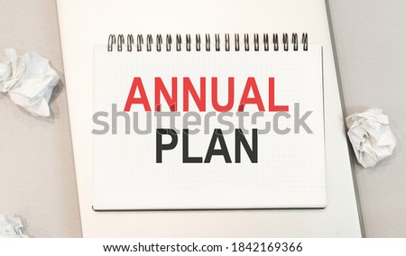 The word annual plan is written in a notebook that sits on a gray desktop along with a laptop. Accounting workplace
