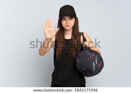 Young Ukrainian sport girl with sport bag isolated on grey background making stop gesture