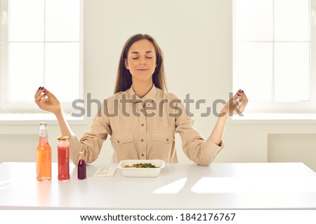 Eat and enjoy life. Happy relaxed young business woman meditating with eyes closed and reaching zen sitting at table with fresh healthy takeaway meal during lunch break at home or in sunlit office Royalty-Free Stock Photo #1842176767