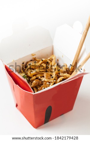 Udon noodles with fried chicken and vegetables in the cardboard box with wooden chopsticks on the white background