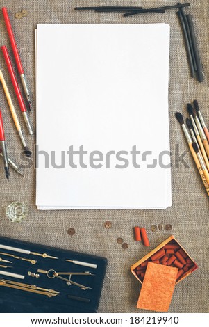 Blank paper sheet on canvas background with color pencils, crayons, chalks, brushes and drawing tools with retro filter effect
