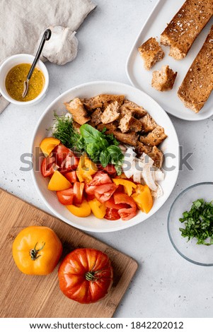 Overhead shot of panzanella bread salad construction with tomatoes, toasted bread, salad dressing and herbs