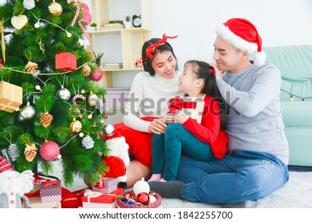 Happy asian parents giving xmas present for their little daughter at living room,decorated by christmas tree.