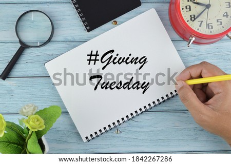 Top view of notebook written with hashtag GIVING TUESDAY with pen and glasses on wooden background with copy space.Flat lay.