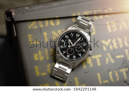 Close up black dial military style wristwatch with stainless steel watch band. Wristwatch for men with military objects in the background.
