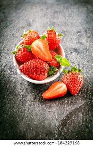 Delicious farm fresh juicy strawberries served in a bowl with whole and halved fruit in a high angle view on dark slate with vignetting