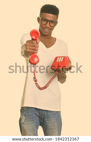 Portrait of happy young handsome African man giving old telephone