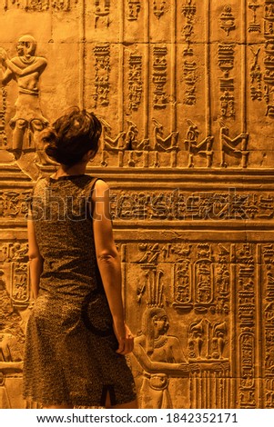 A young woman looking at Egyptian drawings and hieroglyphs at the Temple of Kom Ombo, the temple dedicated to the gods Sobek and Horus. In the town of Kom Ombo near Aswer, Egypt. Royalty-Free Stock Photo #1842352171