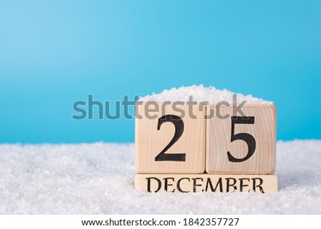 Closeup photo picture of wooden calendar showing the 25th of december standing on white soft snow