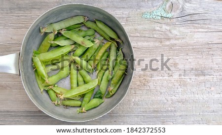 Pea pods in aliminium dish on wooden background, top view