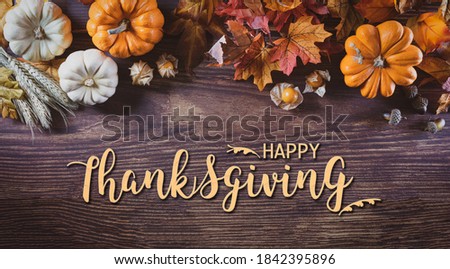 Thanksgiving background decoration from dry leaves and pumpkin on  wooden background. Flat lay, top view with Happy Thanksgivings text.