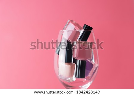 Pink and purple nail polish bottles set. Nail polish bottles in wine glass. Purple nail polsih bottles on pink background.