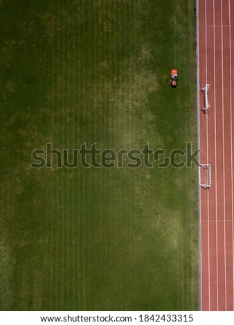 Aerial top down view of man mowing grass on football stadium. Red mower machine and driver. Minimalism. Art drone photography.
