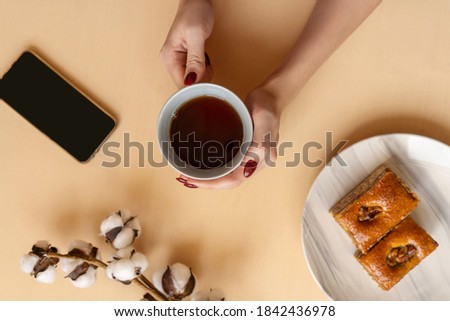 Perfect breakfast: baklava on marble plate and cup of black coffee. Flat lay with cotton plant, phone and hands.