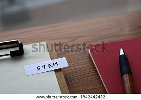 On the desk there is a clipboard, a notebook, and a word book with the word STEM written on it. It was an abbreviation for Science, Technology, Engineering and Mathematics.