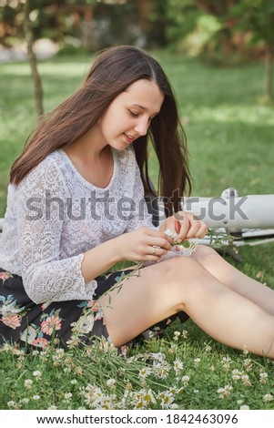 pretty girl with long brunette hair making wreath with camomiles