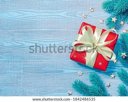 Christmas composition. Gift wrapped in red paper tied with a yellow ribbon with a bow. Coniferous branches and decorations are nearby. Blue wooden background. Flat lay, top view, copy space.