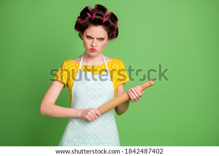 Photo of pretty angry young girl roller hairdo threatening look hold rolling pin ready punish husband called lunch not tasty wear dotted apron shirt isolated green color background Royalty-Free Stock Photo #1842487402