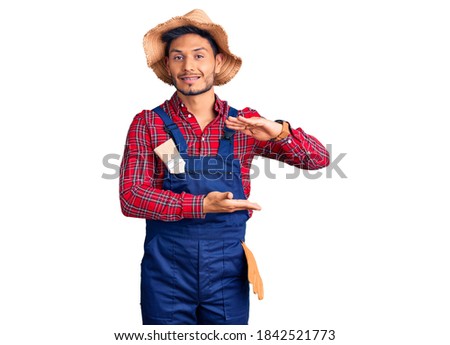 Handsome latin american young man weaing handyman uniform gesturing with hands showing big and large size sign, measure symbol. smiling looking at the camera. measuring concept. 