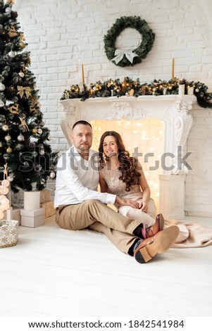 Merry Christmas. Young couple celebrating Christmas at home near fireplace. Happy young couple sitting at home near christmas tree. Picture of young couple hugging in Christmas time