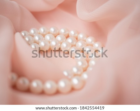 Woman necklace of natural pearls on pink gentle chiffon fabric as background. Luxury  wedding background. Macro shot of bride   jewelry. Soft and delicate wavy pastel material Royalty-Free Stock Photo #1842554419