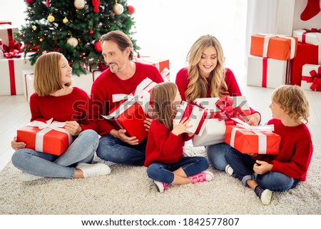Photo of full family five people gathering three small kids sit carpet exchange big boxes present wear red jumper jeans in living room x-mas tree garland many gifts indoors