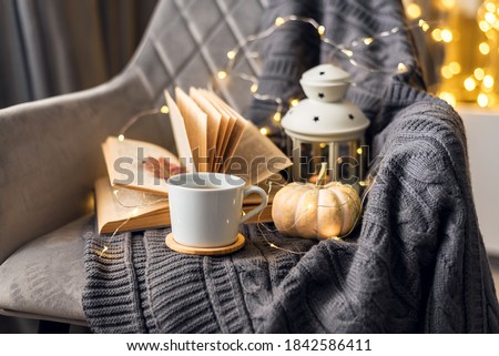 Cozy home interior. A knitted blanket lies on a soft gray chair with a book and a cup of coffee. Home holiday concept on a cold winter day.