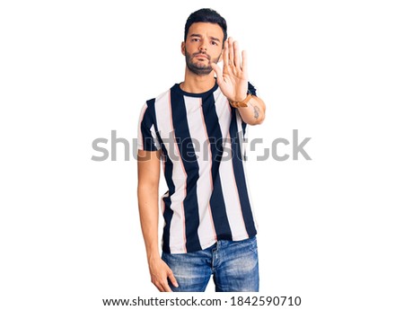 Young handsome hispanic man wearing striped tshirt doing stop sing with palm of the hand. warning expression with negative and serious gesture on the face. 