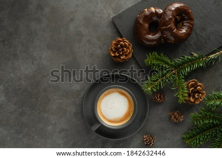A photo of cappuccino and chocolate donuts with Christmas decorations around and space for text. Grey background and cup 