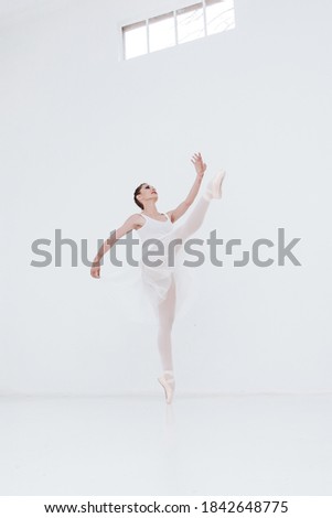 beautiful prima ballerina dancing and jumping in white studio with large window
