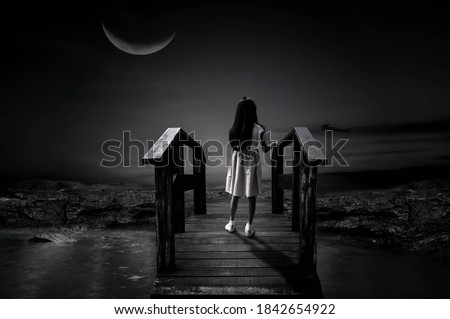 A picture of white little girl standing alone on a wooden bridge in the half moon night.