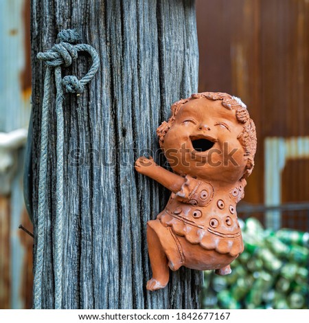 Cheerful clay sculpture of a girl on a wooden post. Blurred background.