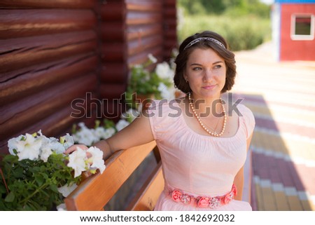 Beautiful Ukrainian lady, young, attractive, smiling face girl in a dress is posing for an outdoor photo shoot. Flowers, trees, stones, and other stuff in the background, summer sunny day