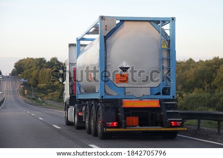 Gray semi truck tanker with 80/2586 dangerous class sign on barrel drive on asphalt highway on a summer day on green trees background, Arylsulfonic acids ADR hazardous cargo logistics, rear view