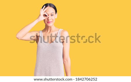 Beautiful brunette young woman wearing casual dress smiling happy doing ok sign with hand on eye looking through fingers 