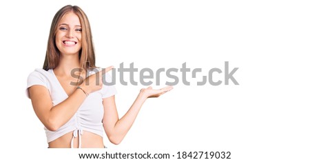 Young beautiful blonde woman wearing casual white tshirt amazed and smiling to the camera while presenting with hand and pointing with finger. 