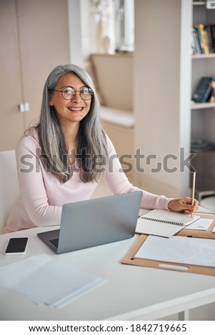 Close up portrait of happy smiling female designer sitting at the work desk while looking and posing at the photo camera in room indoors