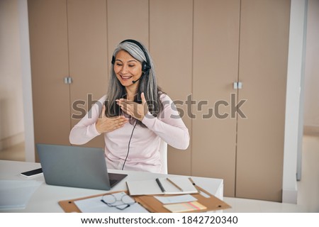 Close up portrait of charming Asian woman learning and communicating in sign language online at a laptop from home office