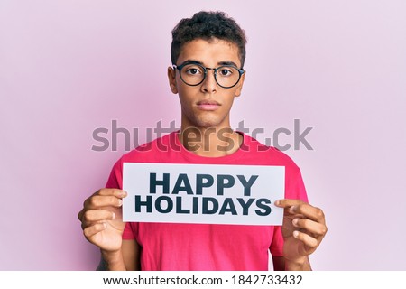 Young handsome african american man holding happy holidays message relaxed with serious expression on face. simple and natural looking at the camera. 
