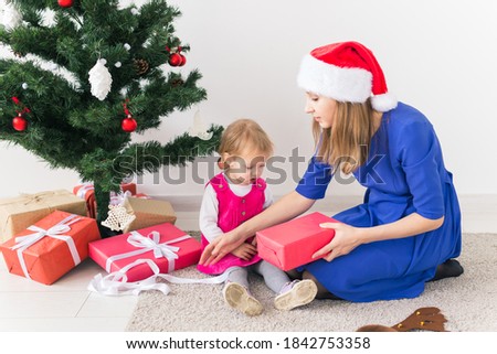 Smiling mother open Christmas presents with baby daughter in room at background. Winter season. Motherhood. Merry Christmas. New Year.