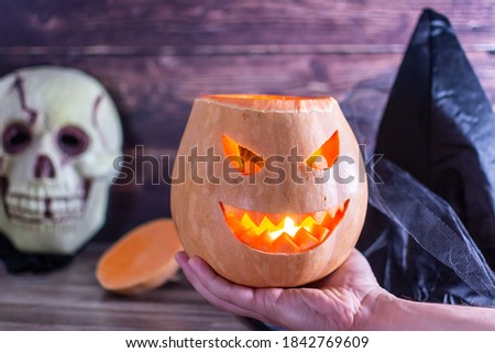 Picture of halloween background with pumpkin and witch hand on wooden table against wooden background. Halloween bokeh background with burning orange pumpkin that a men holds in his hand.
